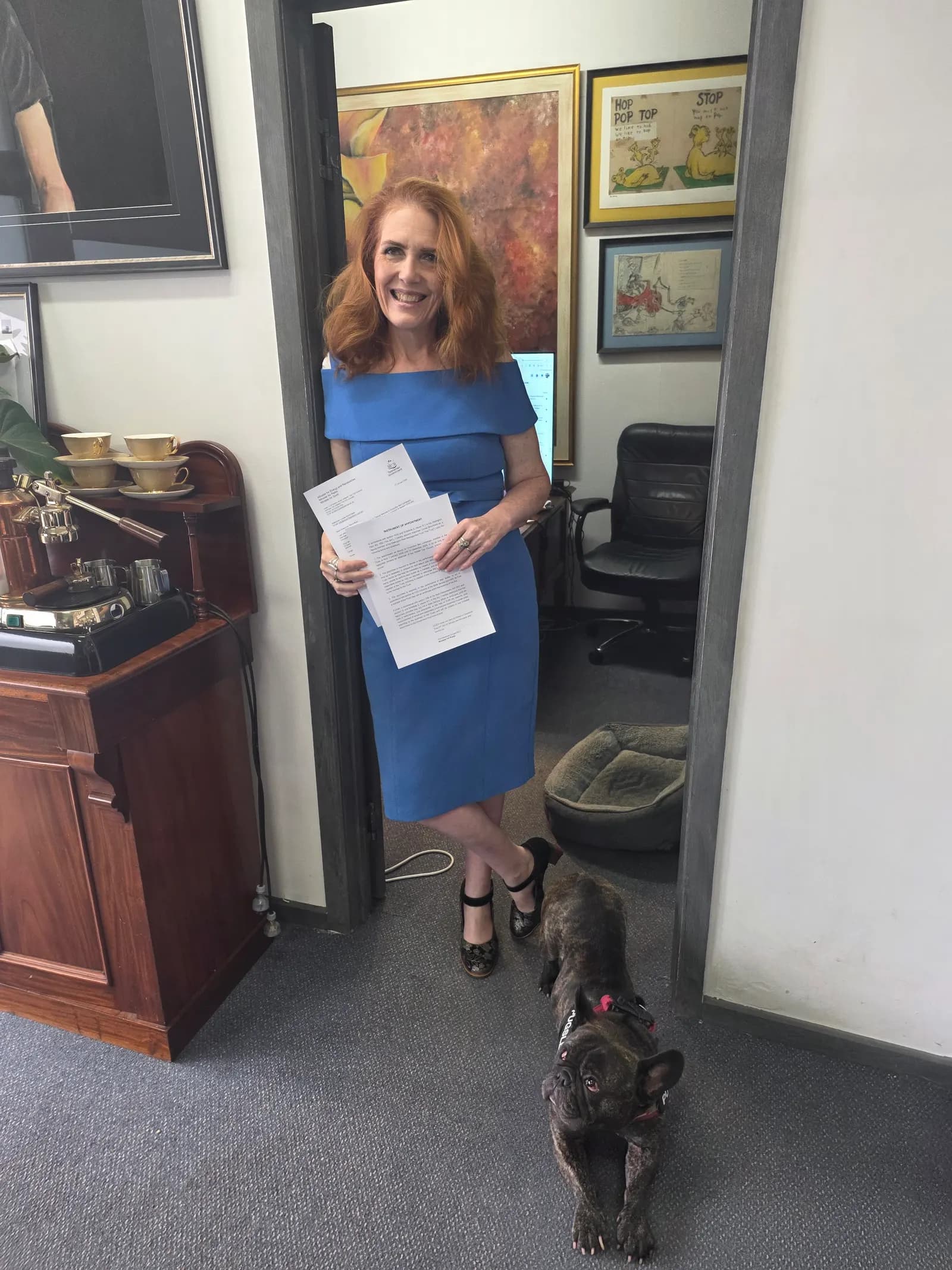 Louise Bloomfield in her Hobart office holding papers, with the office French bulldog beside her
